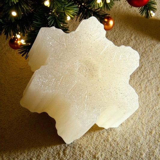 Decorative white snowflake soap on a textured surface with Christmas tree decorations in the background.