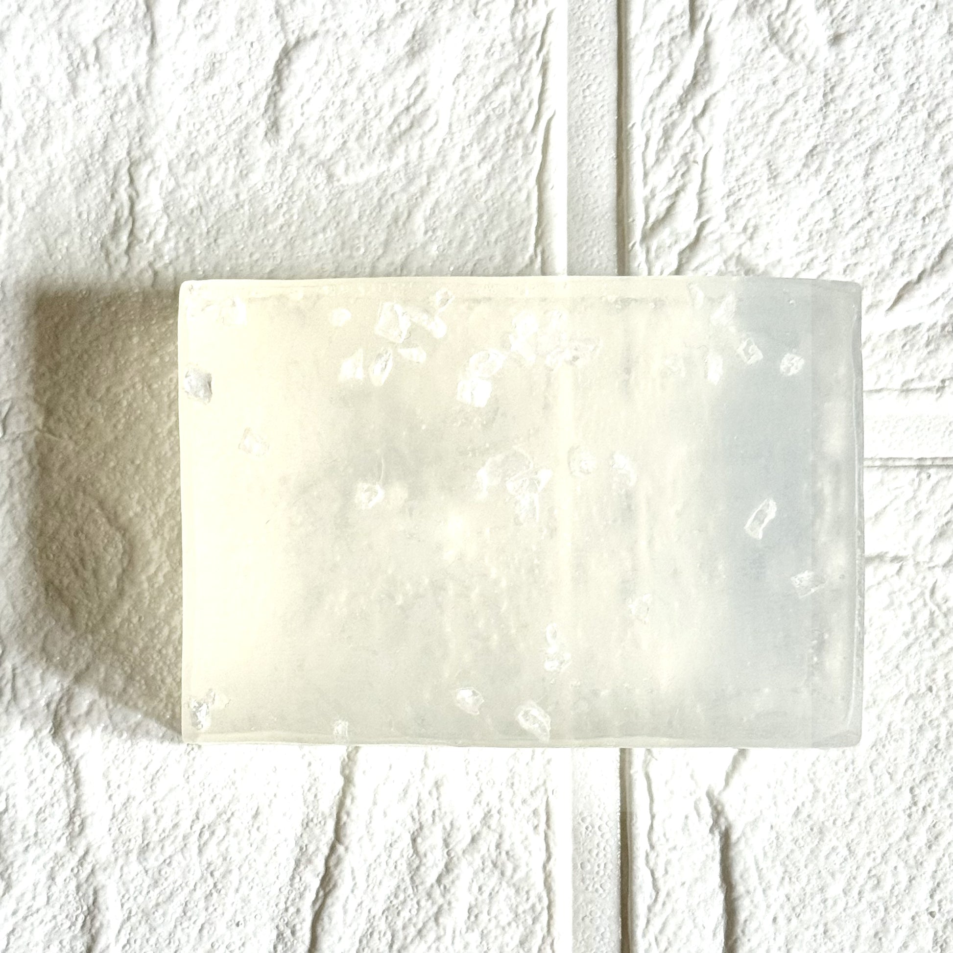 Rectangular transparent bar of soap with sea salt on a textured white background