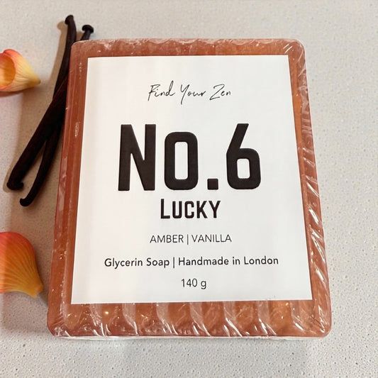 Bar of soap labeled 'No. 6 Lucky' with vanilla beans and flower petals on a light background