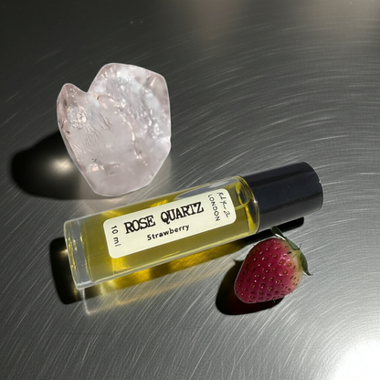 Rose Quartz perfume bottle with strawberry and crystal on a reflective surface