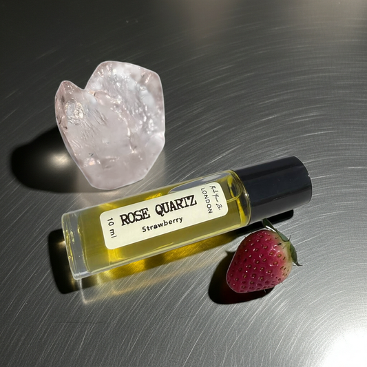 Rose Quartz perfume bottle with strawberry and crystal on a reflective surface