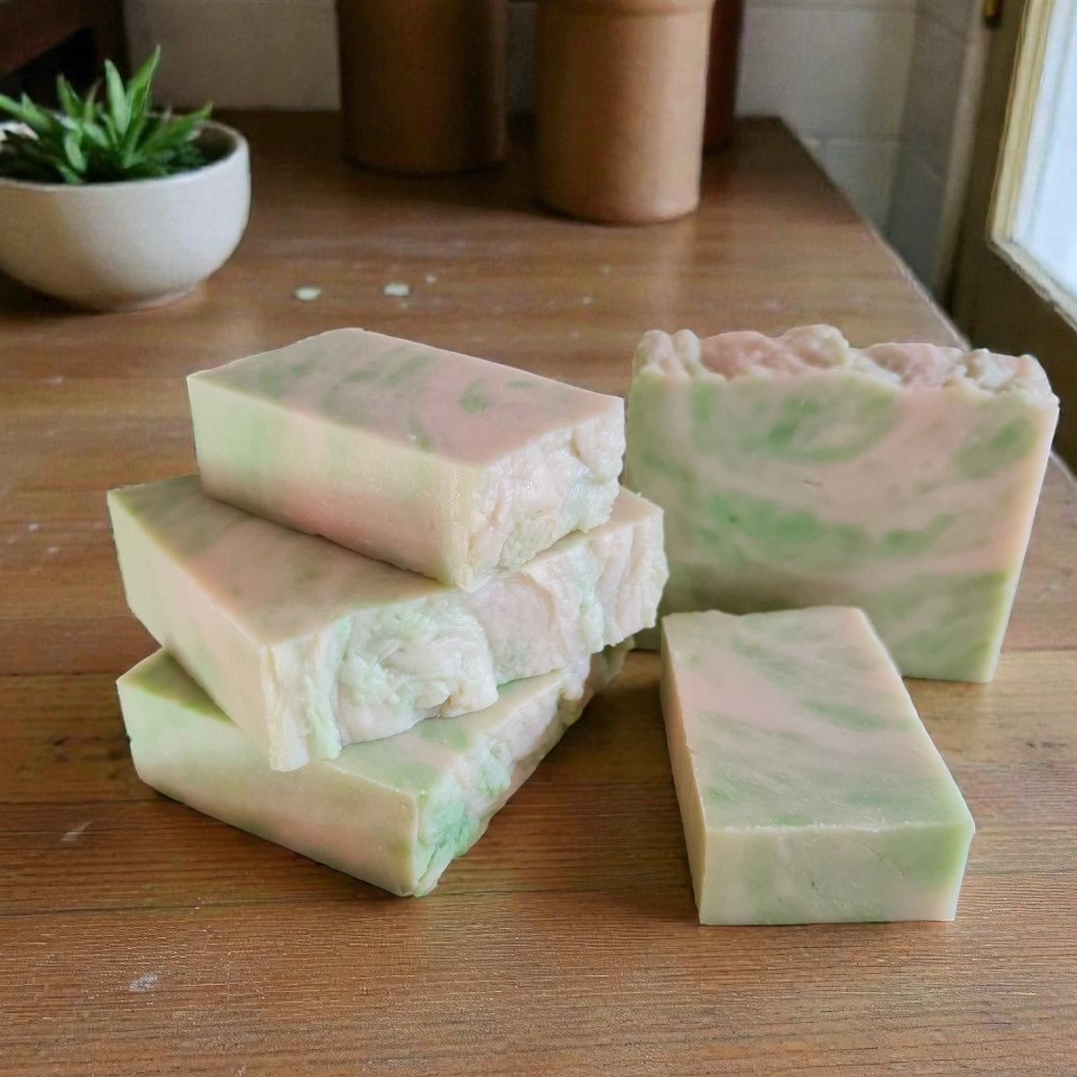Green and white swirled soap bars on a wooden surface with a plant in the background.